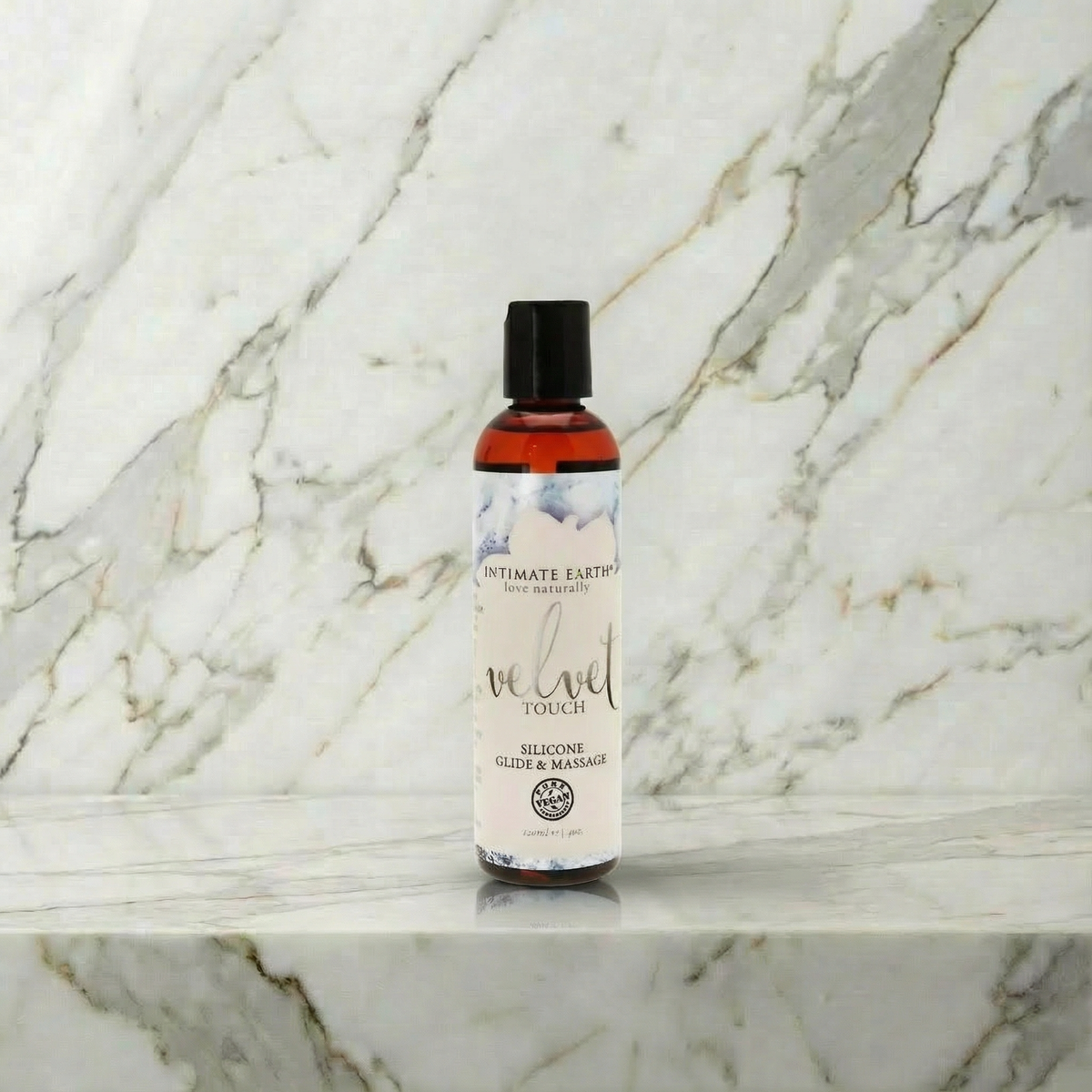 Flesje Intimate Earth Velvet siliconen glijmiddel 120 ml rechtop op een marmeren plank