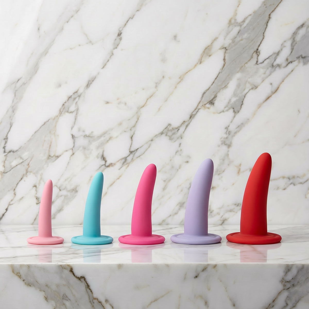 Vijf dilators in oplopende maat, van lichtroze tot rood, op een marmeren plank