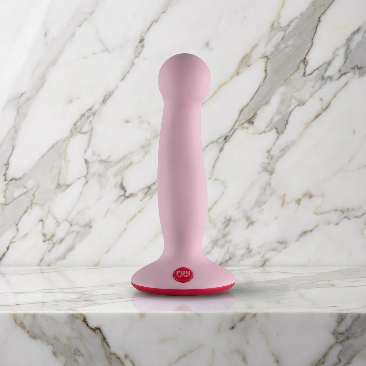Licht roze Fun Factory Amor dildo met rode zuigvoet rechtop op een marmeren plank