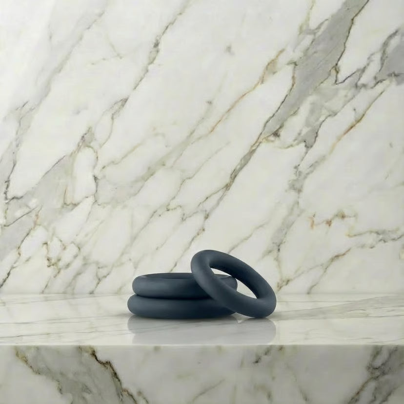All-round Cockring Set: drie donkergrijze siliconen cockringen op een marmeren plank
