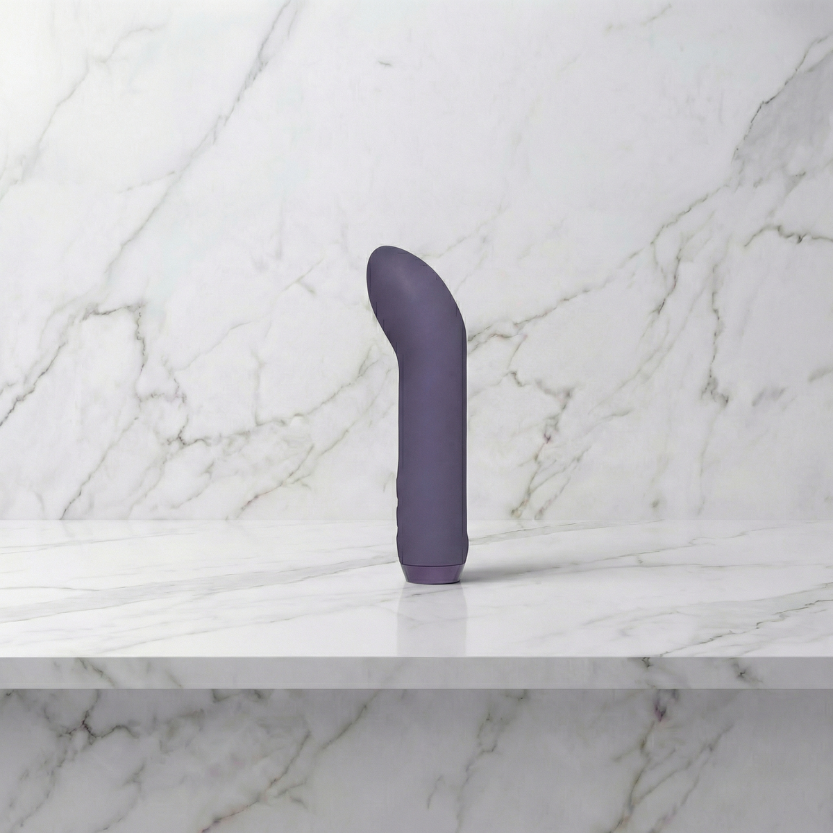 Paarse mini vibrator met gebogen punt rechtop op een marmeren plank, G-Spot Bullet van Je Joue