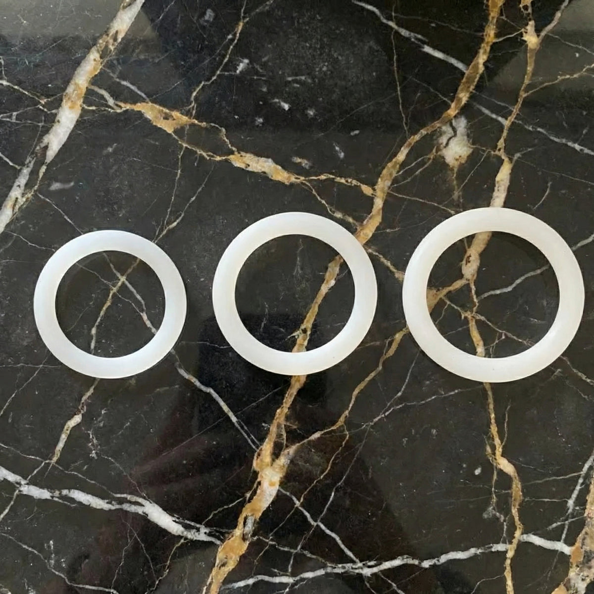 Sfeerbeeld van drie witte siliconen cockringen op donker marmer, White Cockring Set