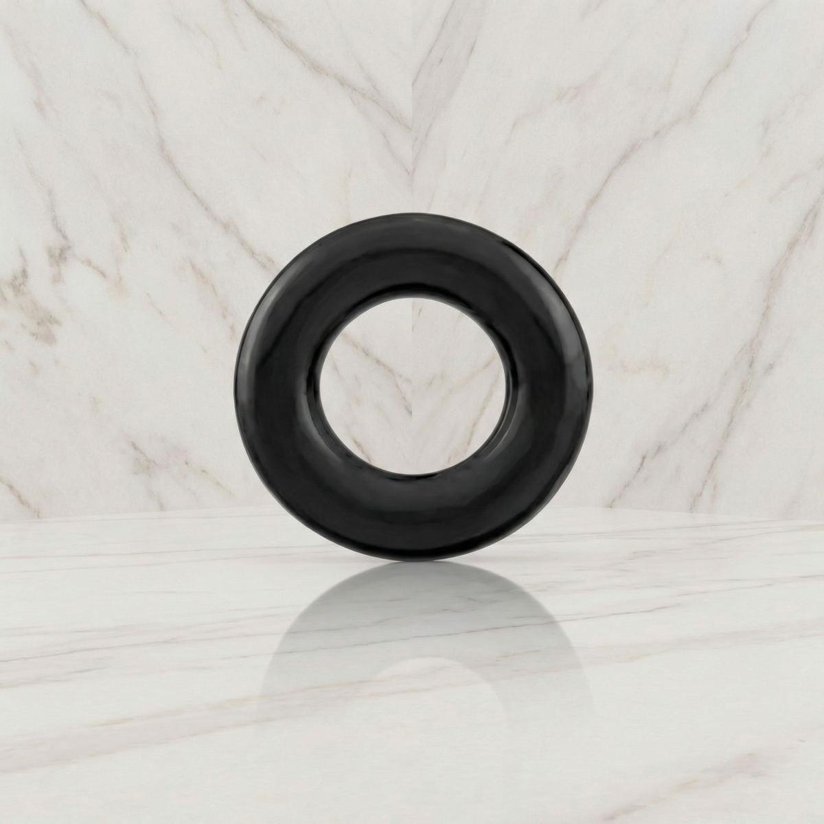 Zwarte cockring rechtop op een marmeren plank tegen een marmeren wand, Kleine cockring