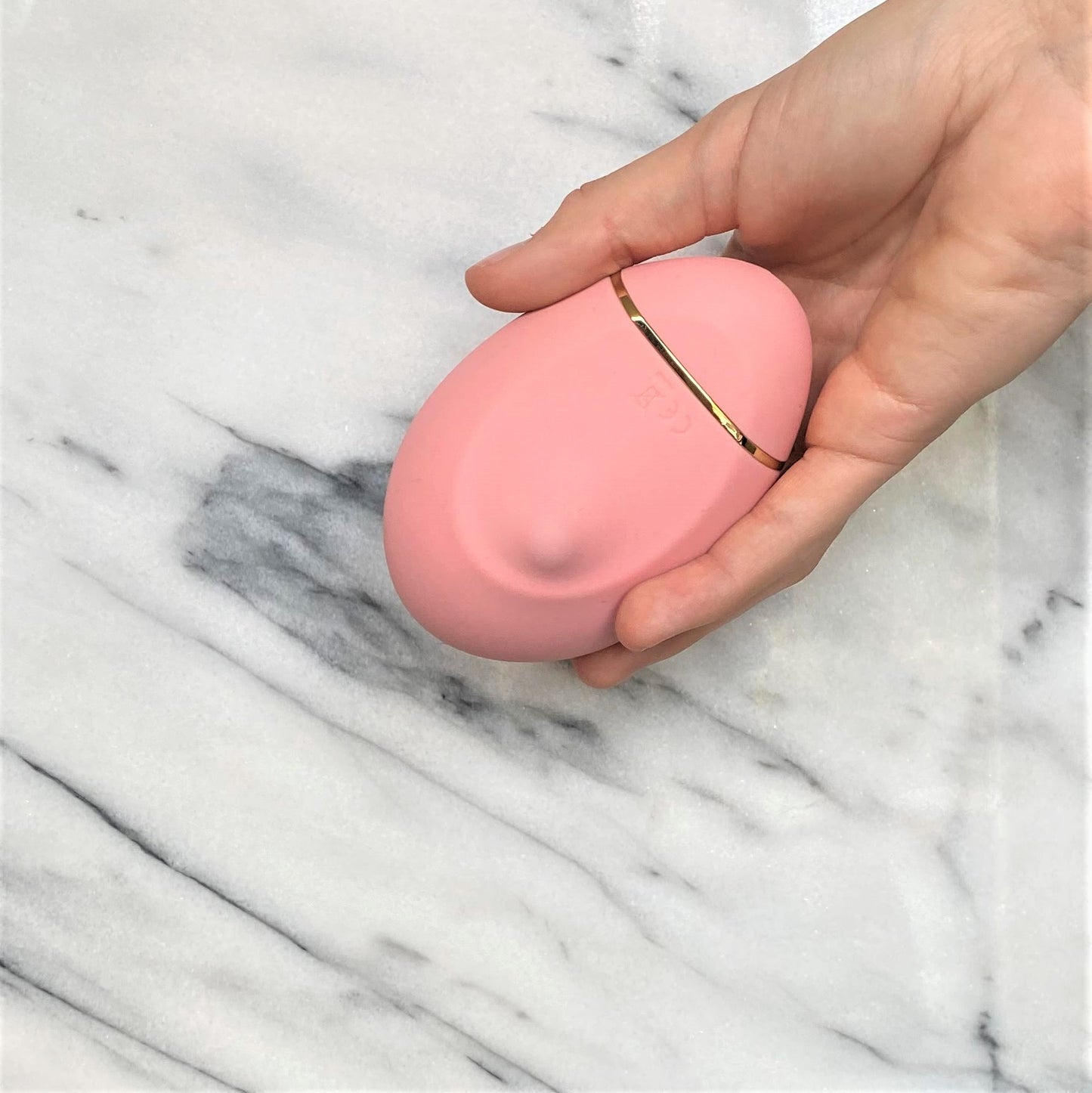 Roze siliconen clitoris vibrator met gouden accent in hand, compact lay-on design