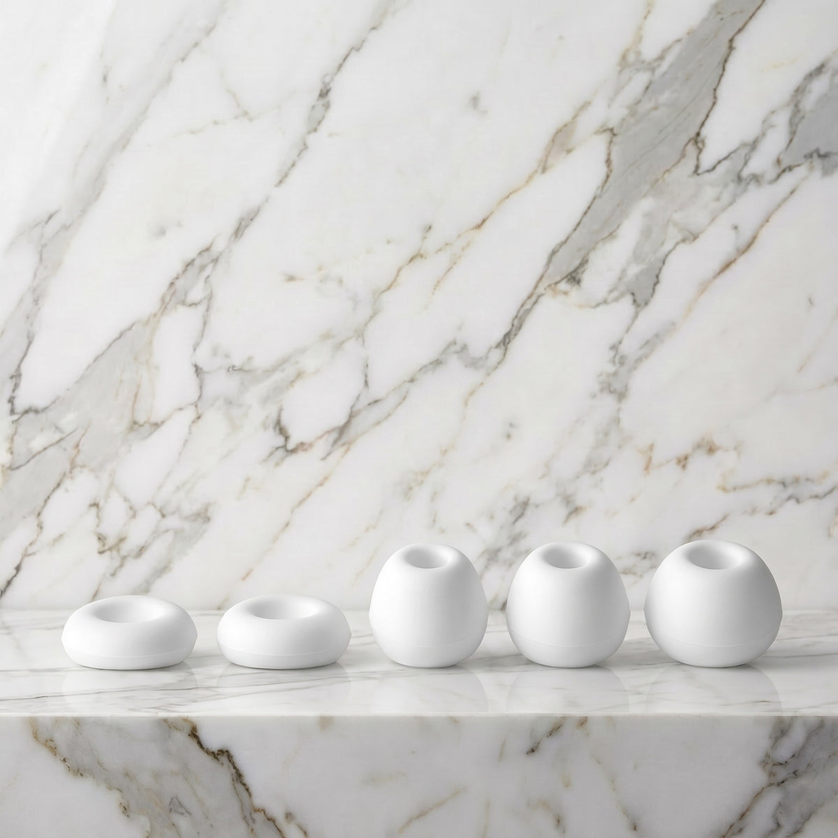 Vijf witte siliconen opzetstukken van de Satisfyer Caps Pro 2 op een marmeren plank