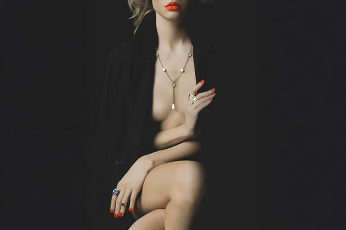 Vrouwelijk silhouet in halfduister, rode lippen en sieraden vangen het licht, een intieme en mysterieuze sfeer overheerst.