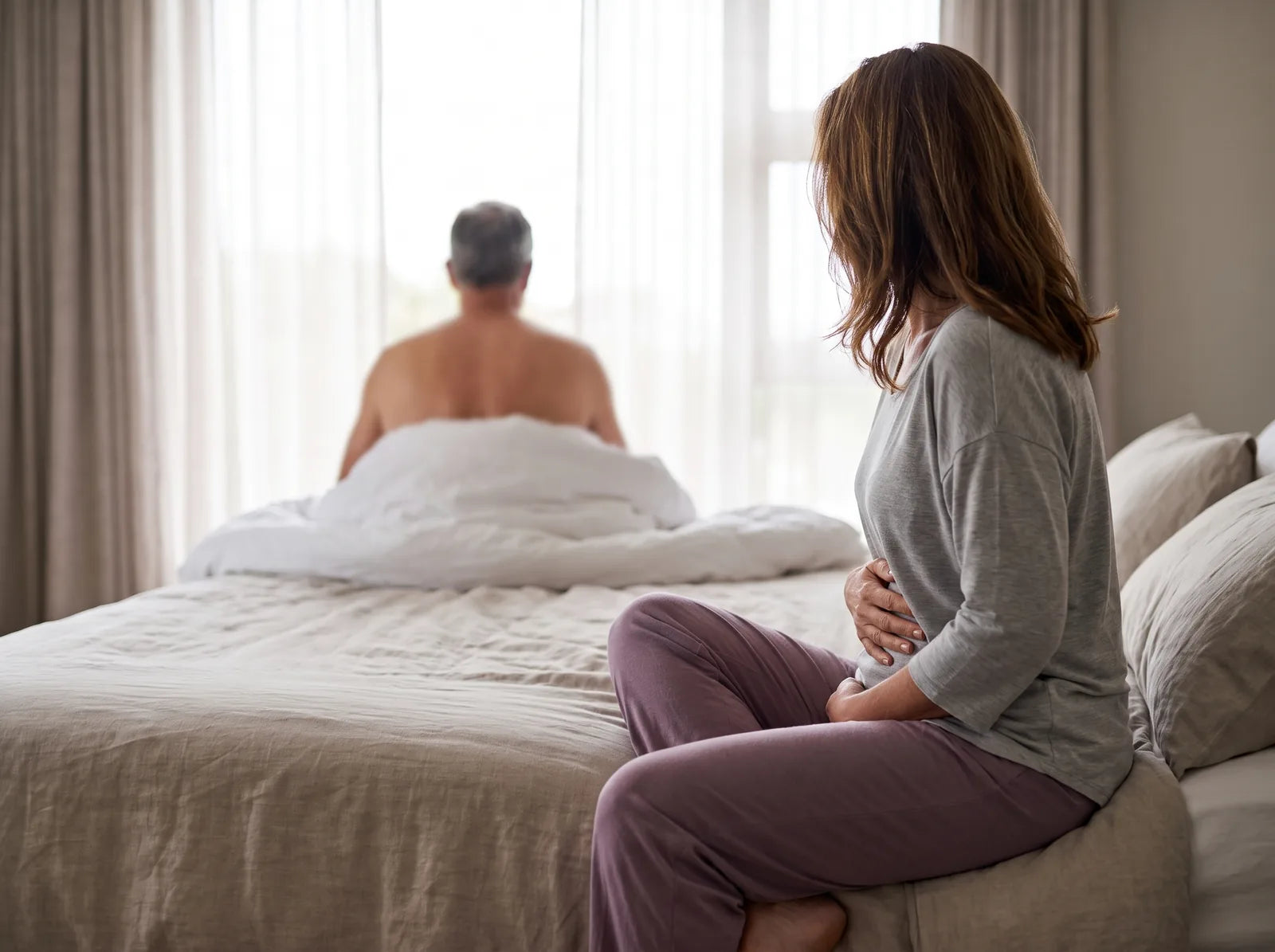 Sfeerbeeld: vrouw op de rand van het bed met een hand op haar buik