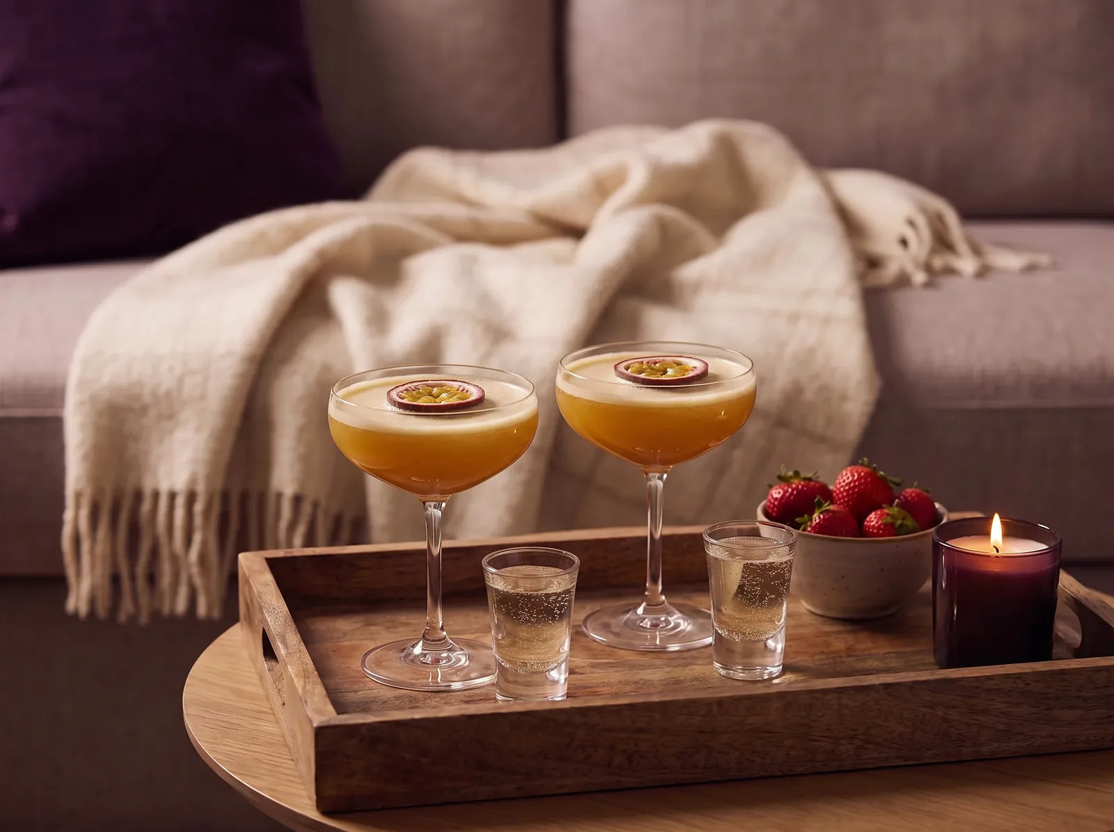 Sfeerbeeld: twee Pornstar Martini's met een halve passievrucht en een shotje prosecco op een houten dienblad bij kaarslicht