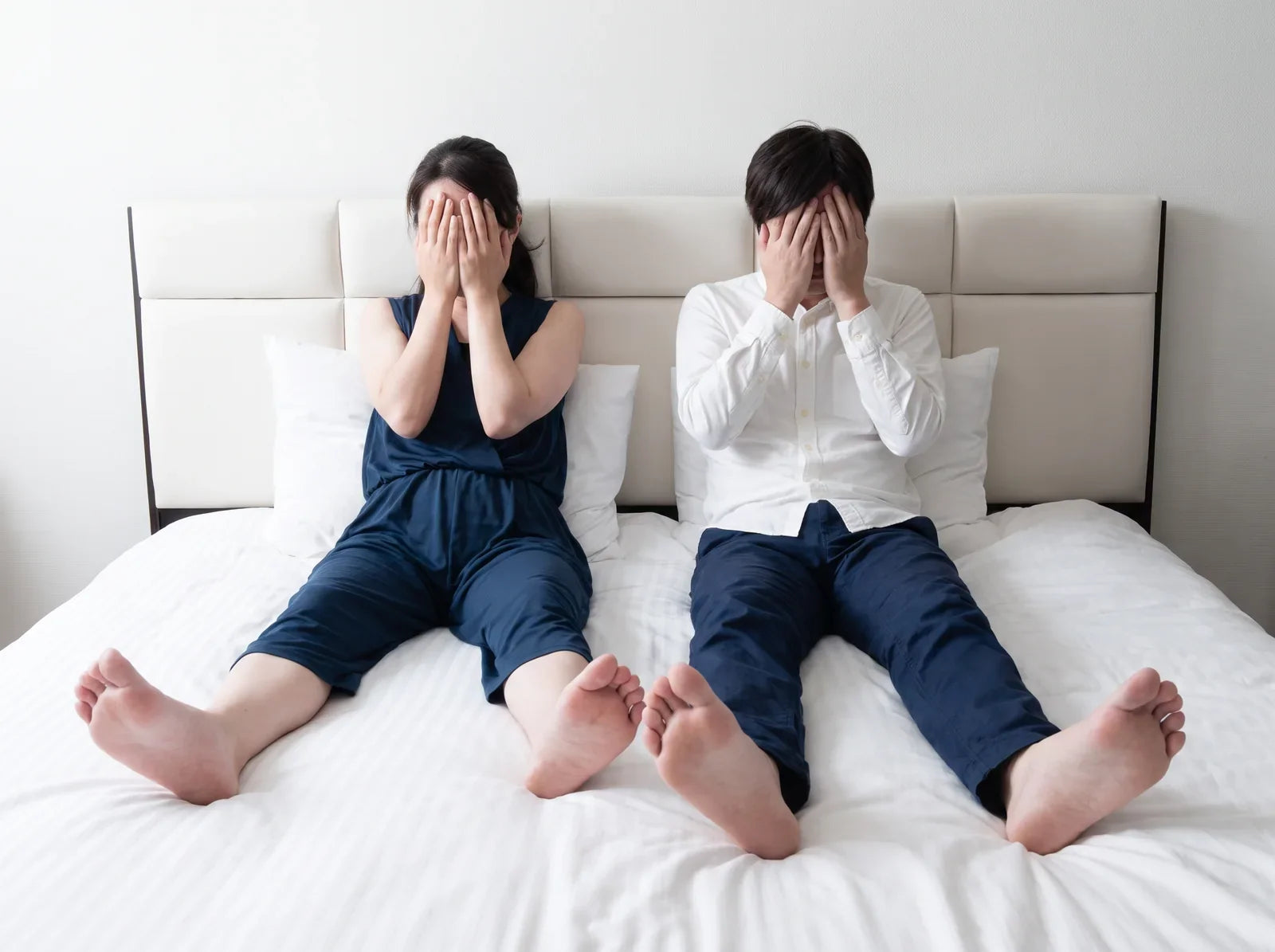 Sfeerbeeld: stel zit naast elkaar op een wit bed met de handen voor het gezicht