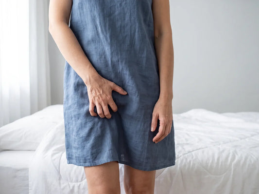 Sfeerbeeld: vrouw in een linnen jurk bij het bed met een hand tegen haar kruis