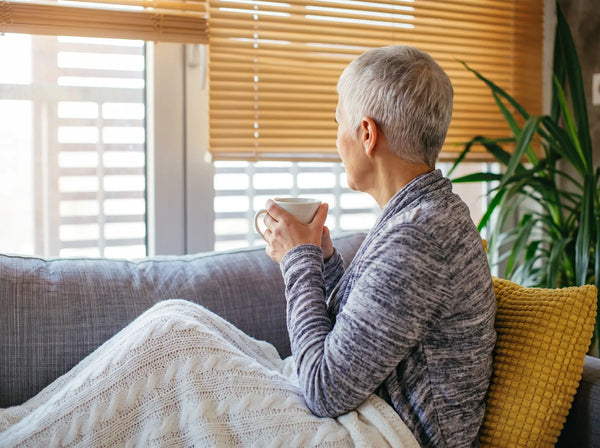 Sfeerbeeld: oudere vrouw van achteren op de bank met een kop thee bij het raam