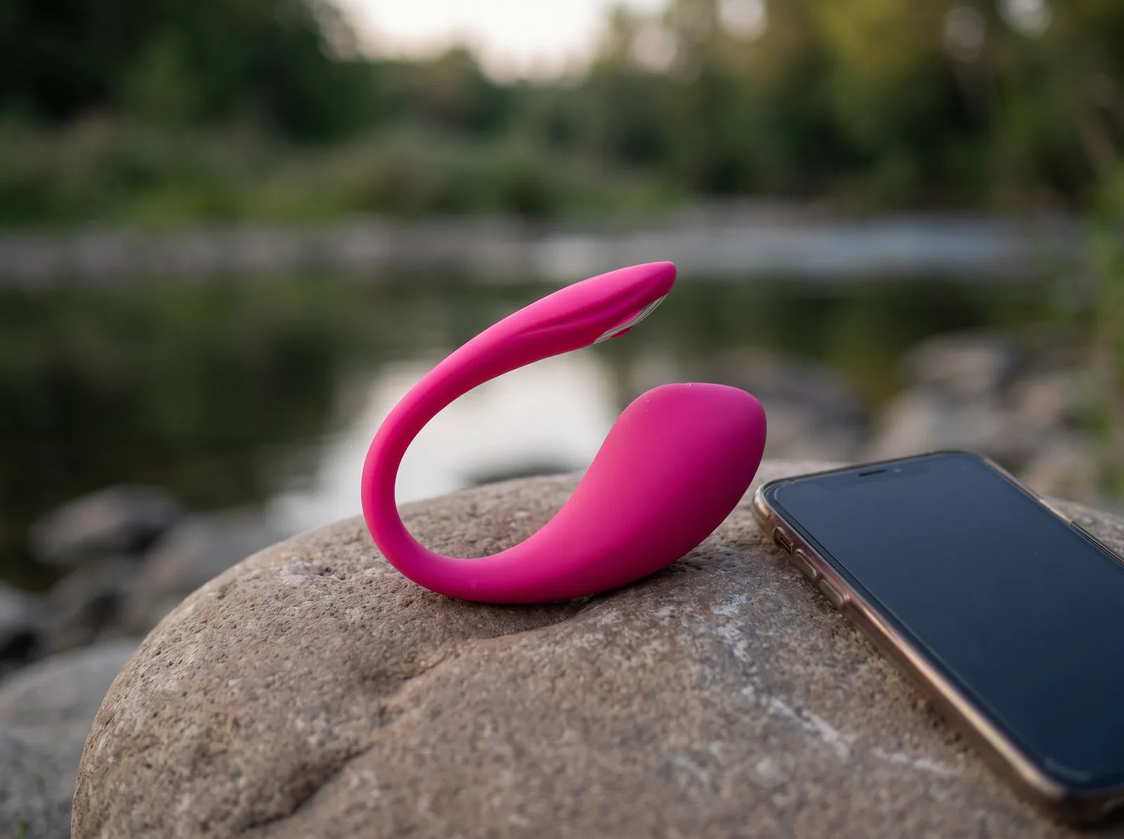 Sfeerbeeld: roze Lovense Lush 4 op een steen aan het water, naast een smartphone