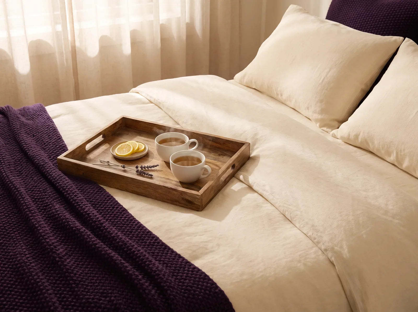 Sfeerbeeld: twee kopjes thee op een houten dienblad op een opgemaakt bed in ochtendlicht