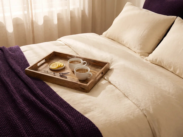 Sfeerbeeld: twee kopjes thee op een houten dienblad op een opgemaakt bed in ochtendlicht