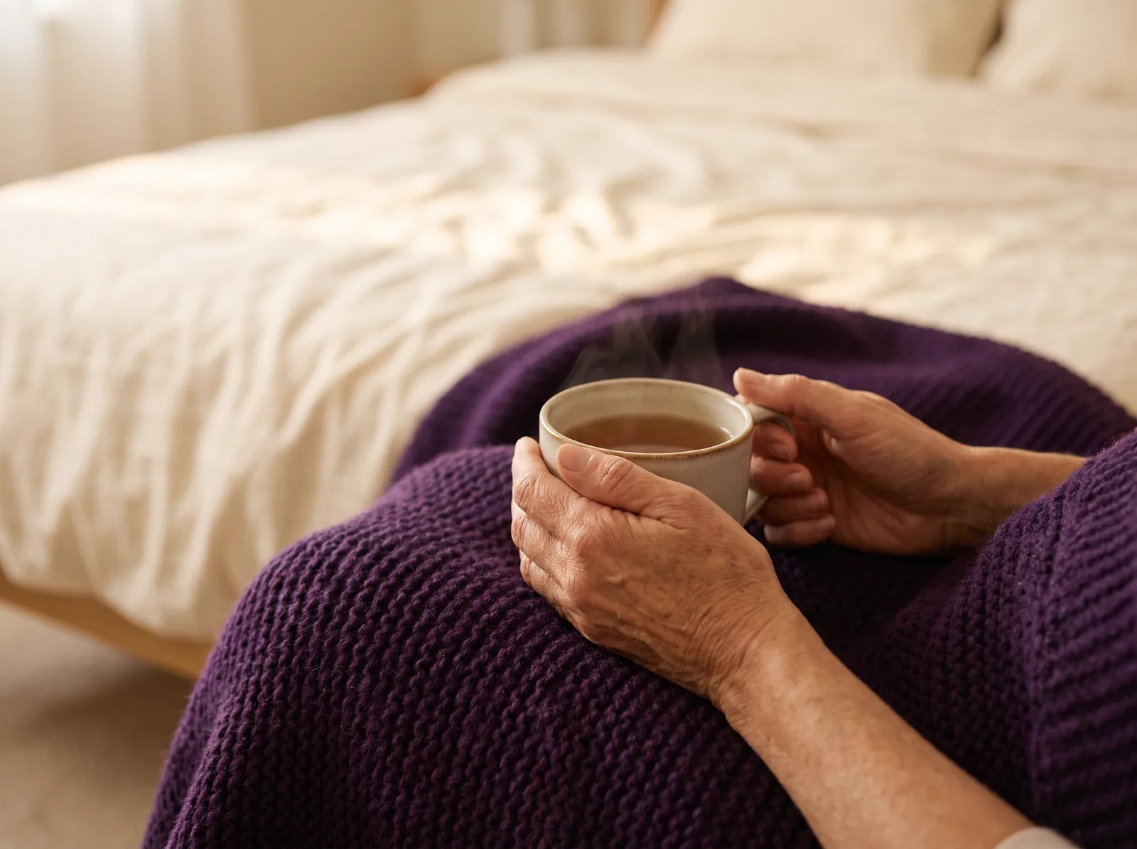 Sfeerbeeld: handen rond een warme kop thee op een paarse plaid op bed