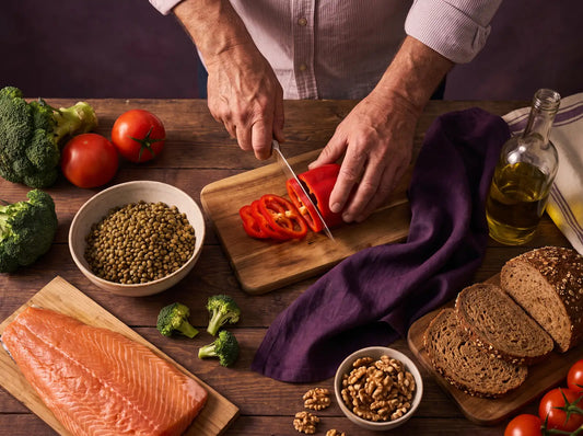 Sfeerbeeld: een man snijdt paprika aan een keukentafel met zalm, linzen, broccoli, walnoten en volkorenbrood