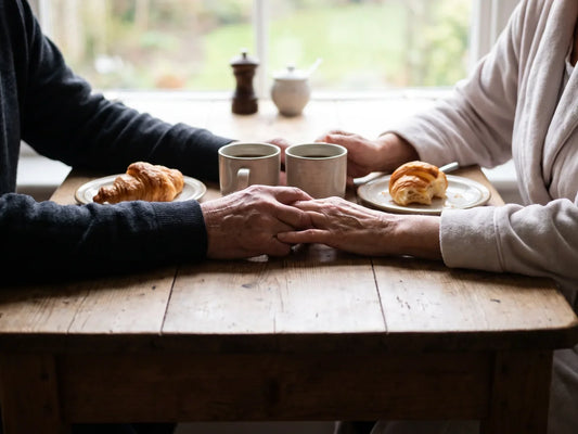 Sfeerbeeld: twee oudere handen houden elkaar vast aan de ontbijttafel, naast twee koffiekopjes