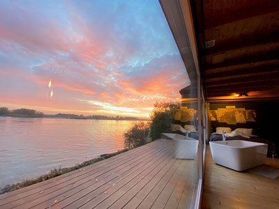 Luxe verblijf aan het water met houten terras en vrijstaand bad bij zonsondergang