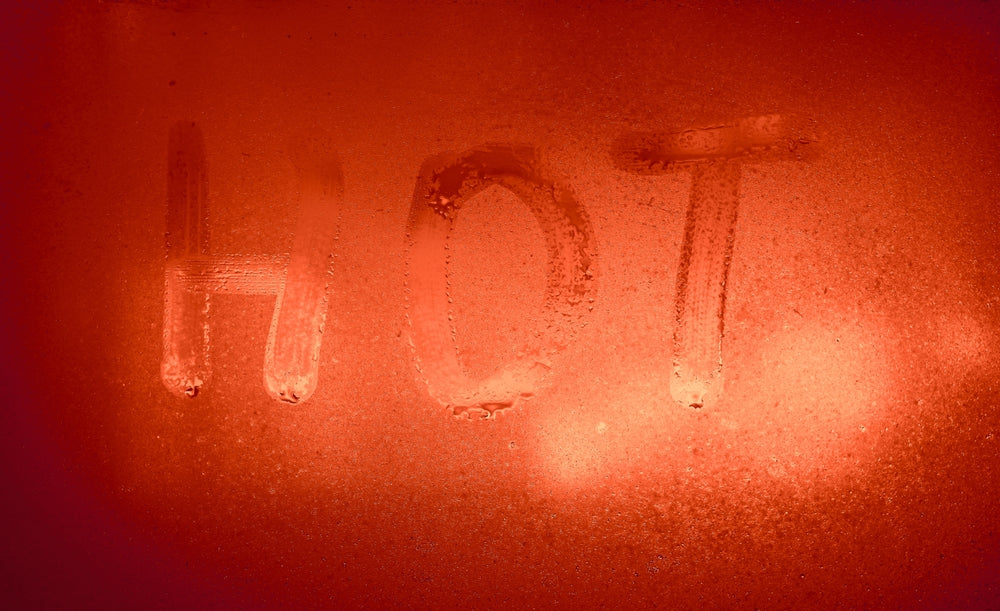 Het woord HOT geschreven op beslagen rood glas in een stoomrijke sauna-sfeer