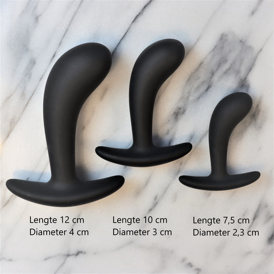 Drie zwarte buttplugs in oplopende maten op een marmeren plank, voor wie begint met anale seks