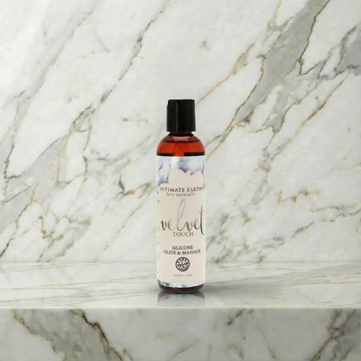 Flesje Intimate Earth Velvet siliconen glijmiddel 120 ml rechtop op een marmeren plank