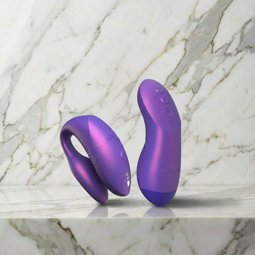 Twee metallic paarse vibrators op marmeren ondergrond: U-vormige koppelvibrator en gebogen clitorisstimulator