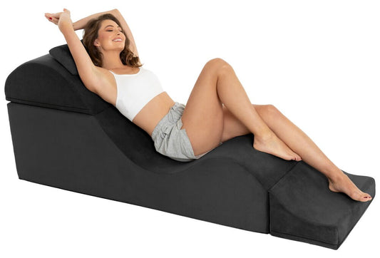 Vrouw ligt languit op de zwarte Liberator Super Aria Flip Chaise in micro-suède, een arm omhoog
