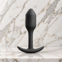Zwarte Snug Plug rechtop op een marmeren plank, buttplug van b-Vibe