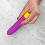Hand met rode nagellak houdt paars-gele ROMP Beat vibrator vast boven marmeren ondergrond
