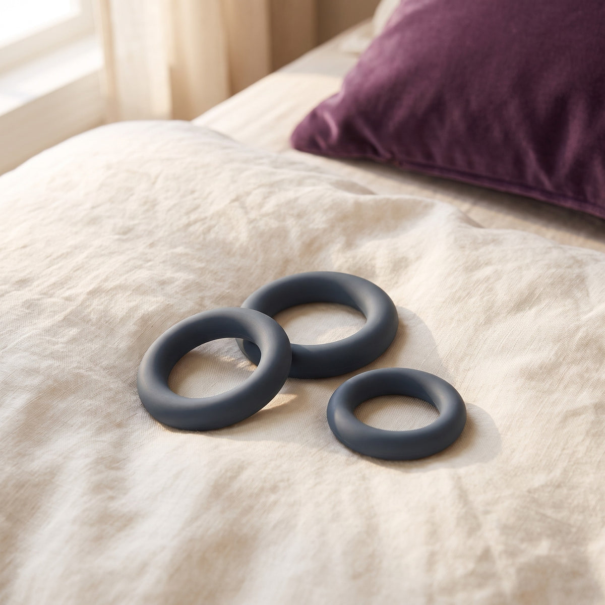 Sfeerbeeld van drie donkergrijze cockringen van de All-round Cockring Set op een linnen dekbed