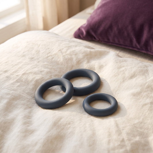 Sfeerbeeld van drie donkergrijze cockringen van de All-round Cockring Set op een linnen dekbed