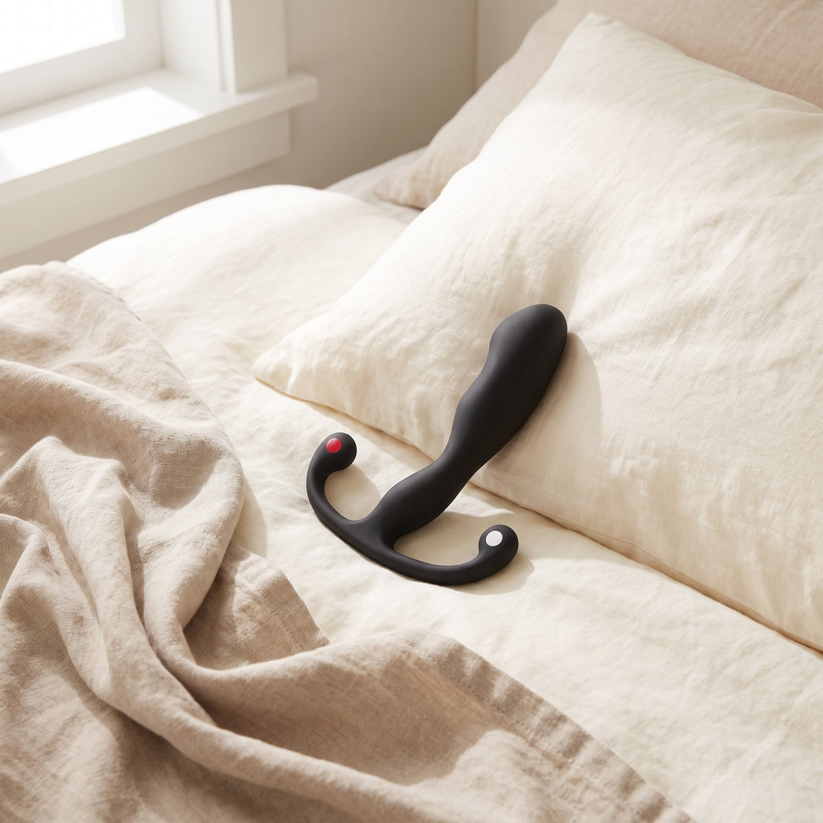 Sfeerbeeld: zwarte Helix Syn prostaatmassager liggend op een opgemaakt bed met creme linnen, Aneros