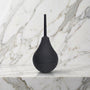 Zwarte anale douche met knijpbol en mondstuk rechtop op een marmeren plank, b-Vibe Anal Shower