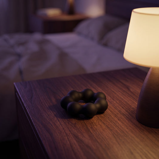 Sfeerbeeld: zwarte Beaded Pleasure Ring op een houten nachtkastje naast een lamp