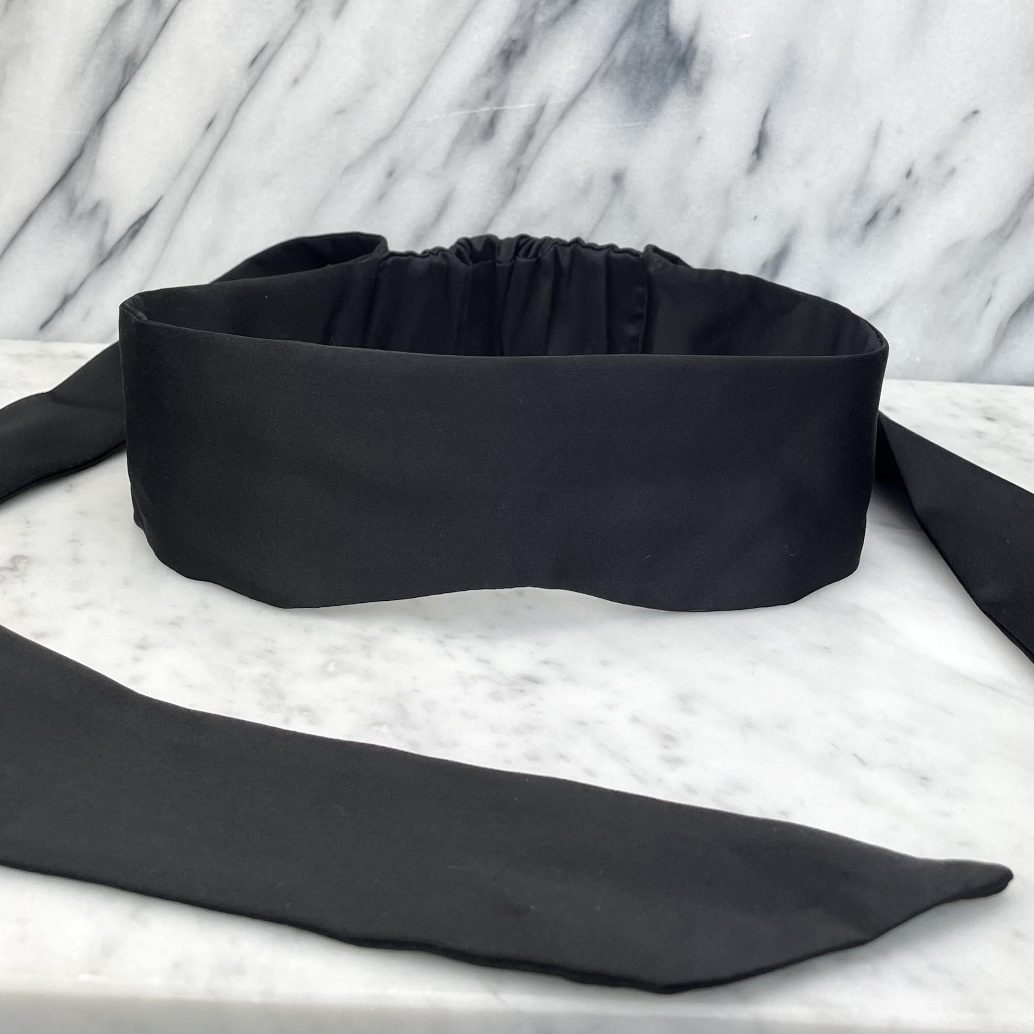 Zwarte satijnen blinddoek met lange striklinten op een marmeren plank