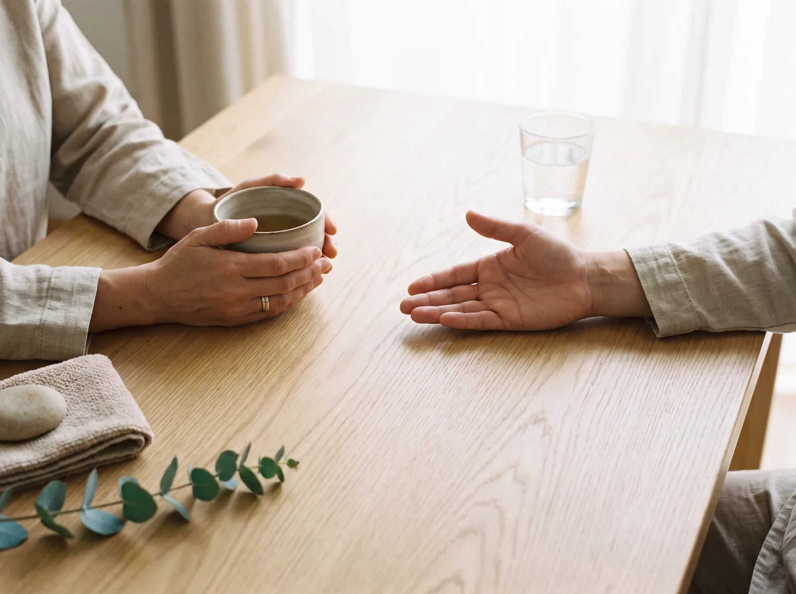 Sfeerbeeld: handen om een kop thee tijdens een rustig gesprek aan een houten tafel