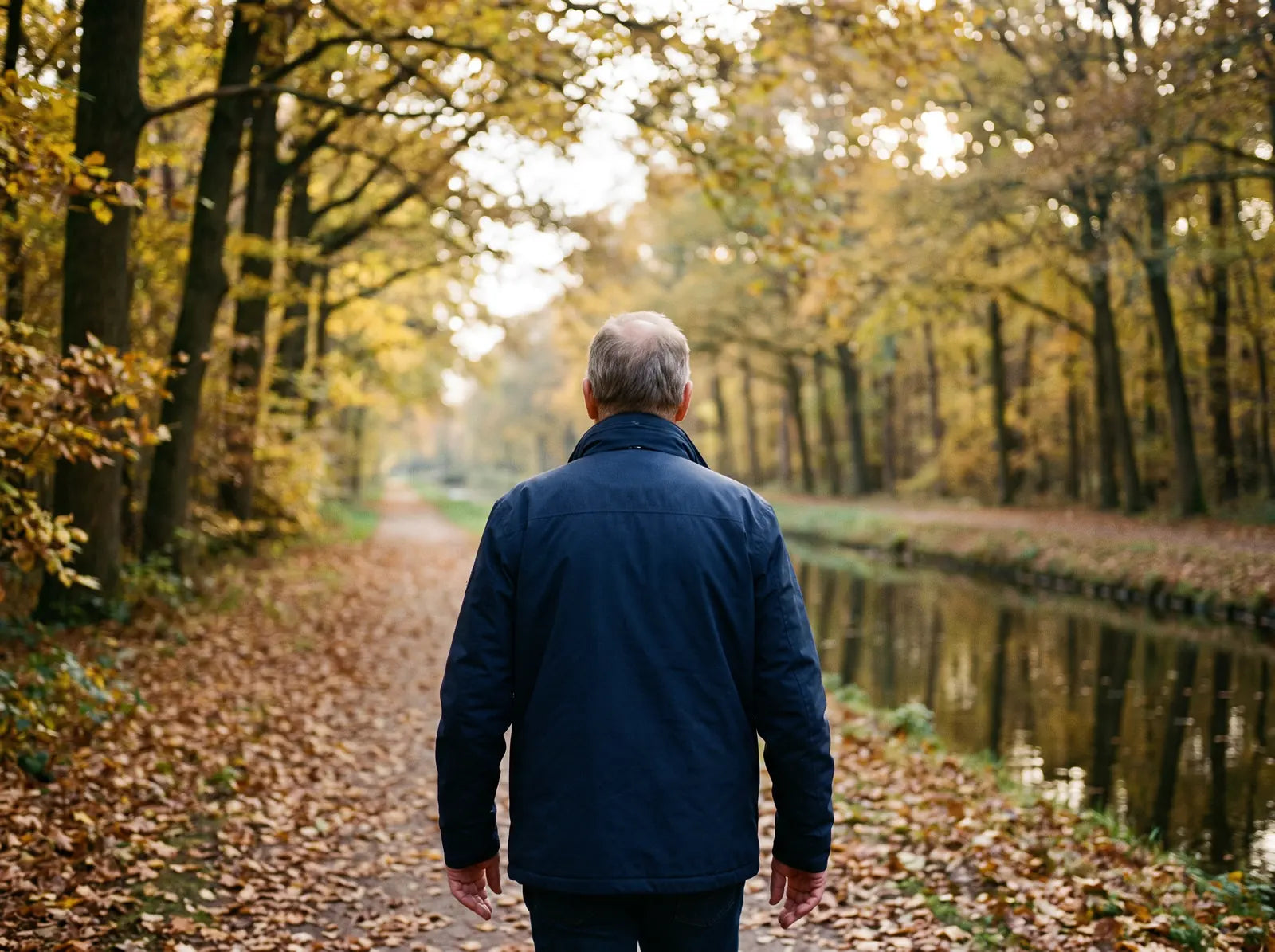 Sfeerbeeld: man van achteren gezien op een herfstig wandelpad langs het water