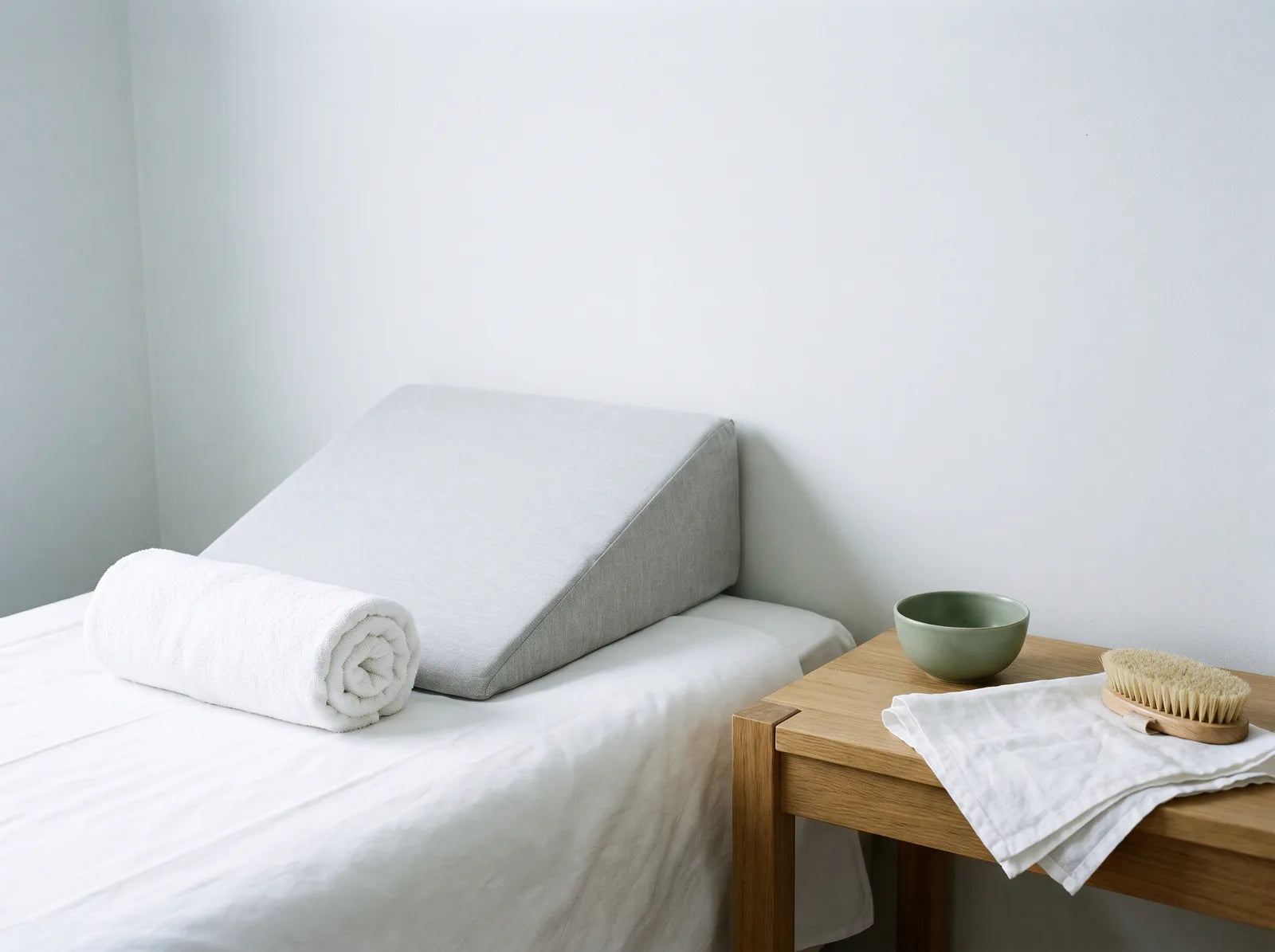 Sfeerbeeld: wigvormig kussen en een opgerolde witte handdoek op een opgemaakt bed