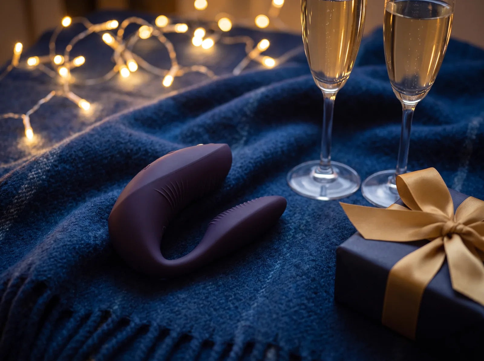 Sfeerbeeld: paarse We-Vibe Chorus Pro op een blauwe plaid met twee champagneglazen en kerstlichtjes