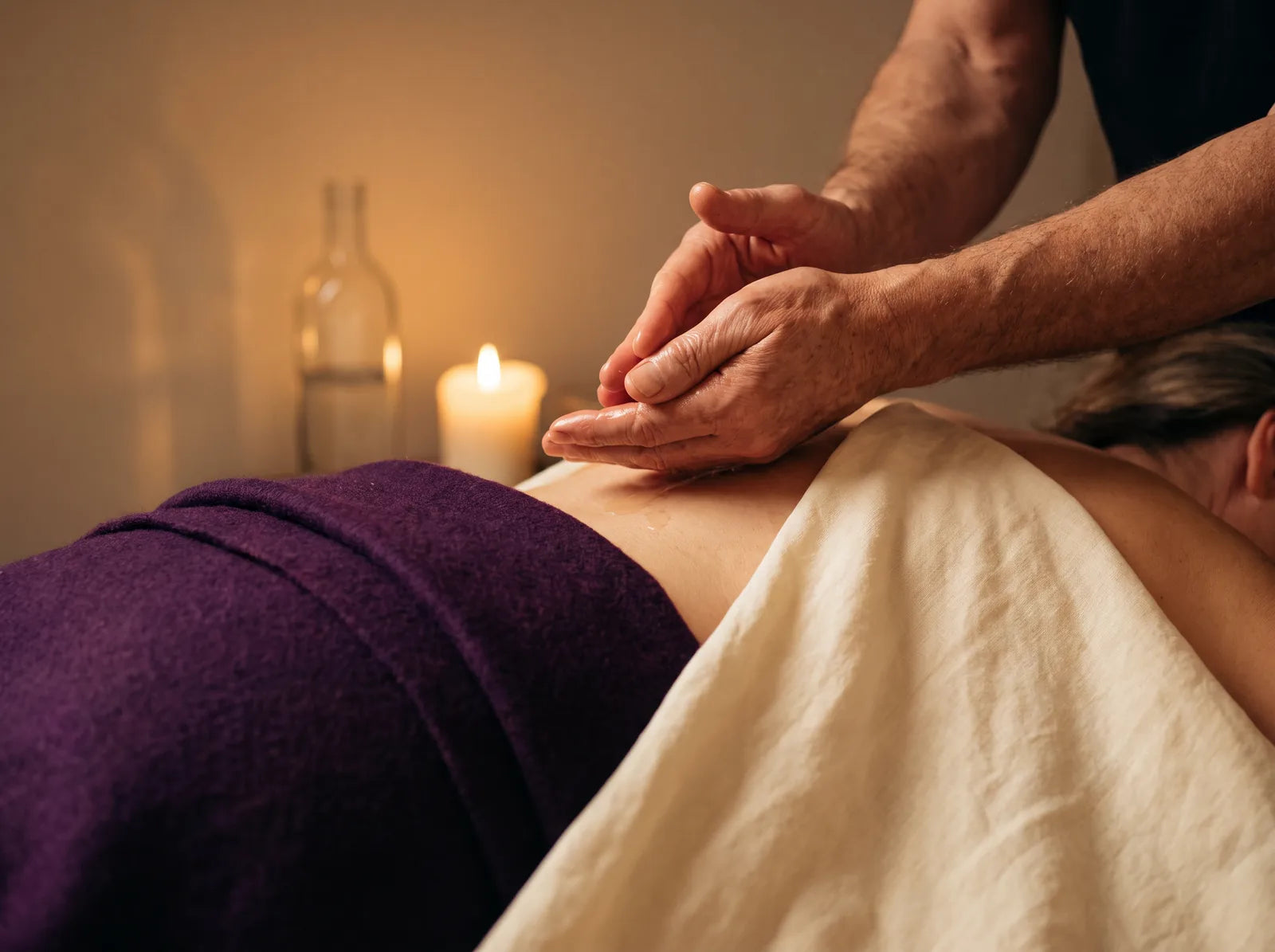 Sfeerbeeld: de handen van een man warmen massageolie op voor een rugmassage bij kaarslicht