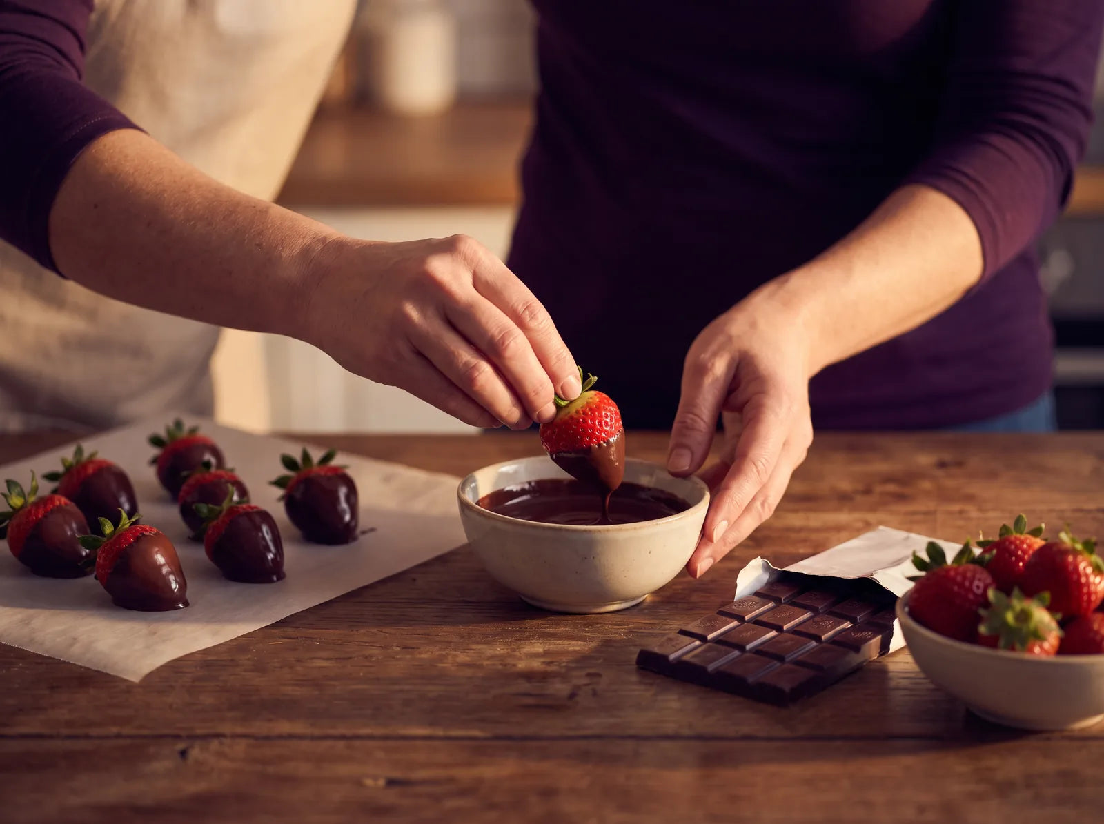 Sfeerbeeld: handen dopen een verse aardbei aan het kroontje in gesmolten pure chocolade