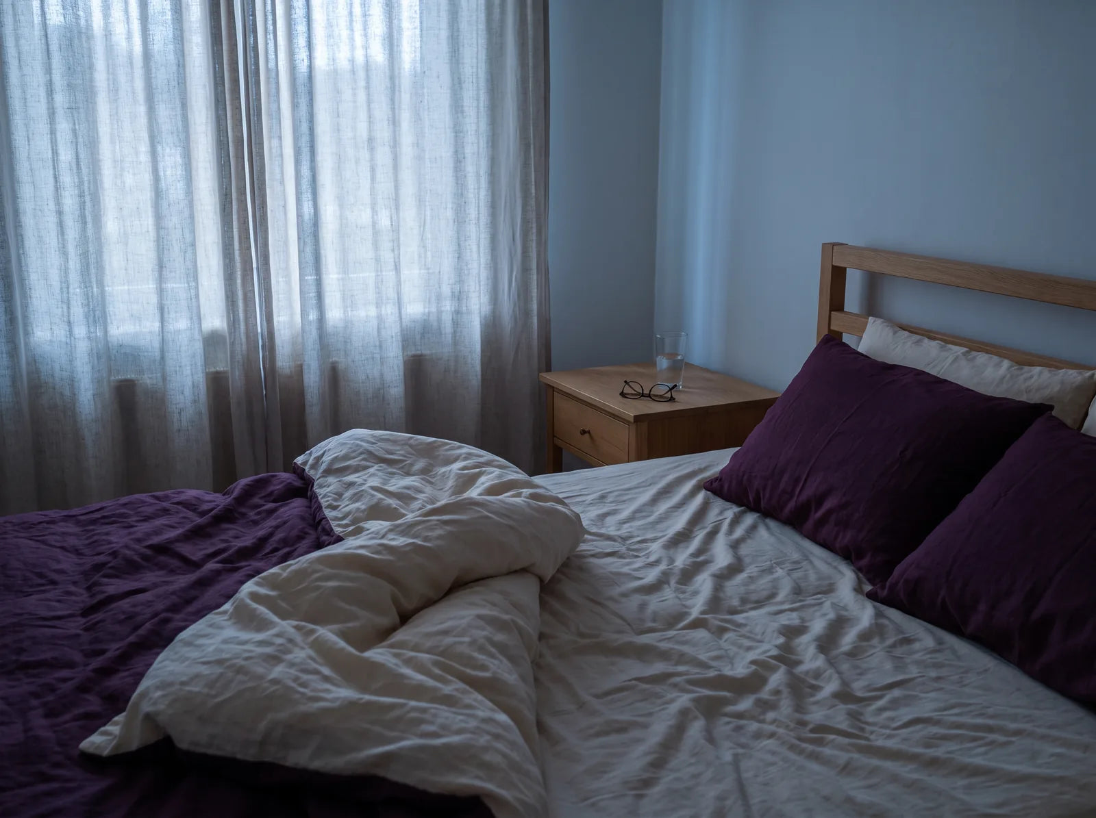 Sfeerbeeld: een beslapen bed in de schemering, met een glas water en een bril op het nachtkastje