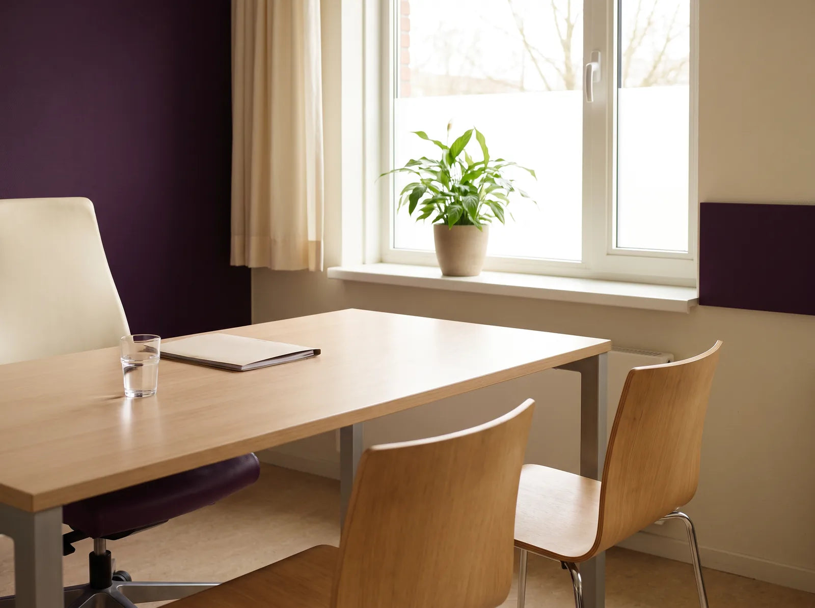 Sfeerbeeld: een lege spreekkamer met een bureau, twee stoelen, een plant en een glas water