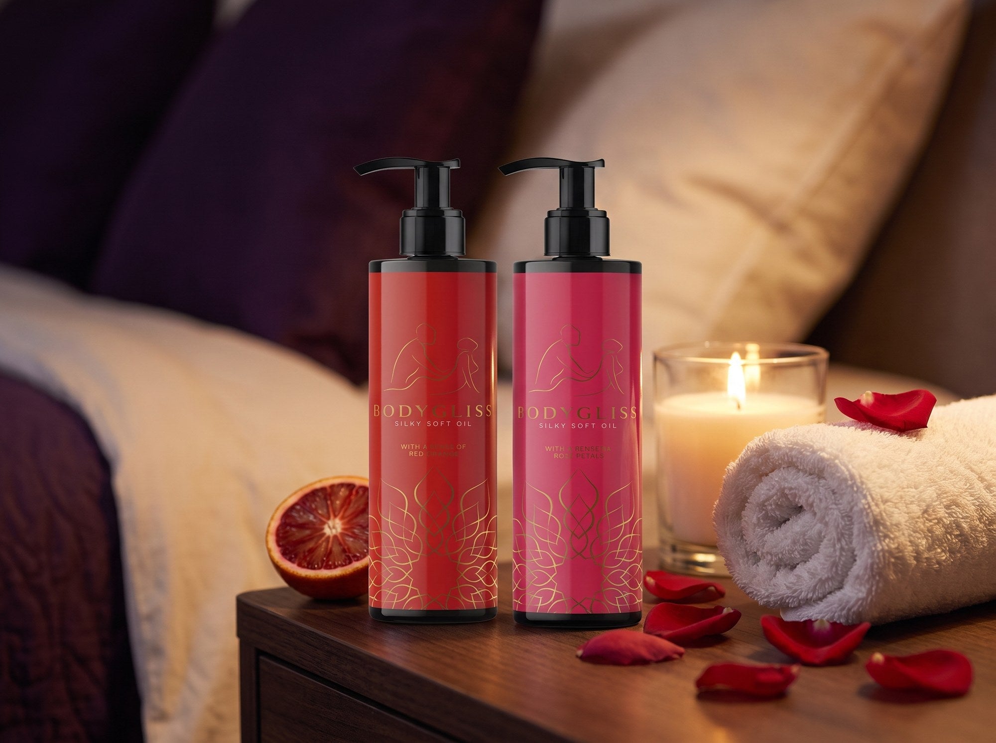 Sfeerbeeld van twee flessen Body Gliss massageolie, Red Orange en Rose Petals, op een nachtkastje met kaars, handdoek en rozenblaadjes