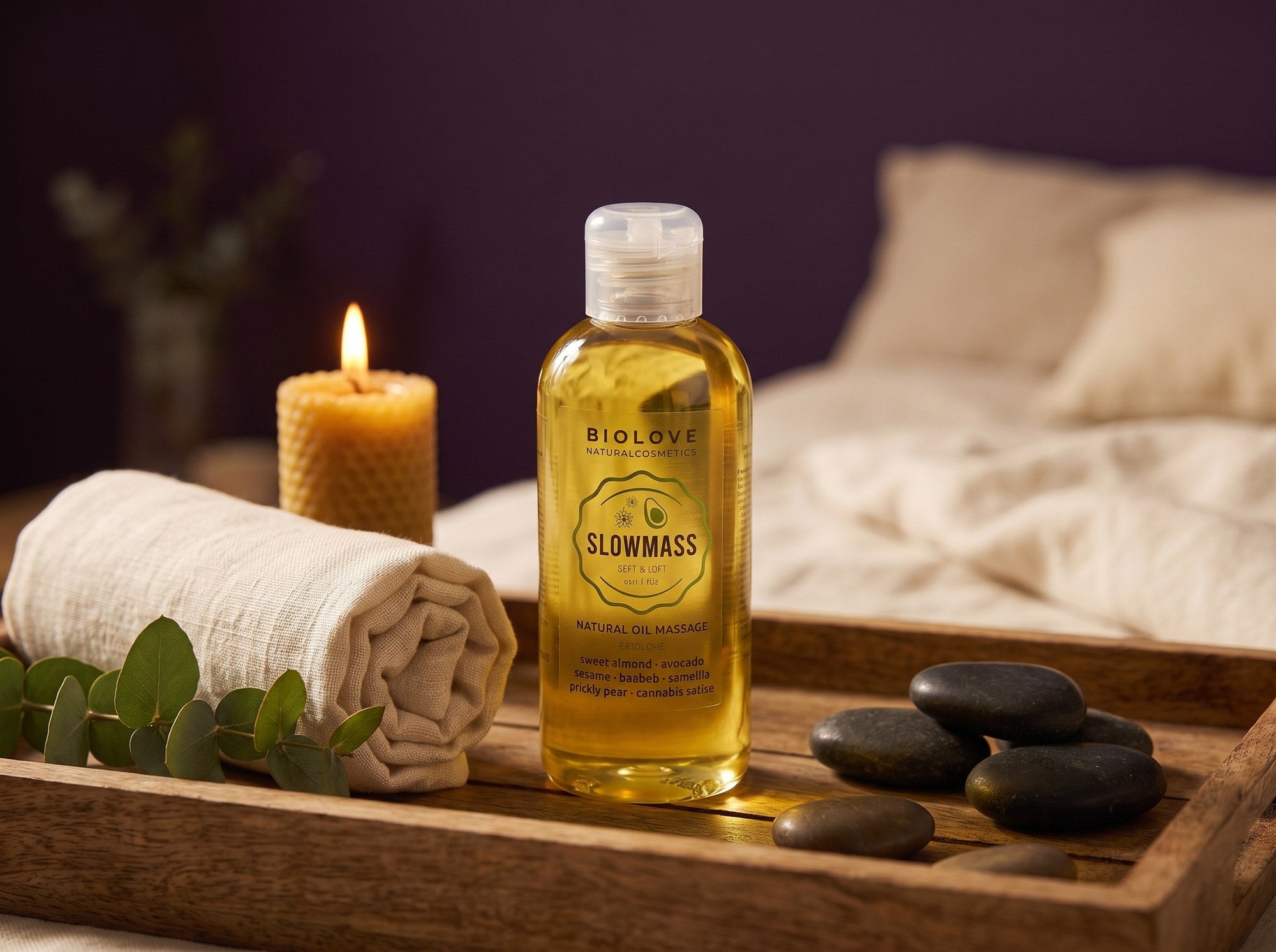 Sfeerbeeld van de fles Slowmass natuurlijke massageolie op een houten dienblad met handdoek, eucalyptus en stenen