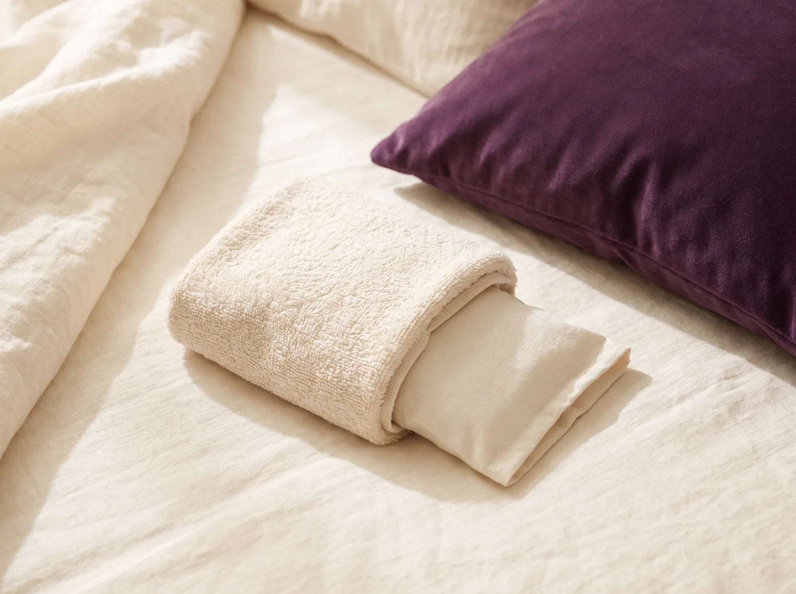 Sfeerbeeld: een coldpack gewikkeld in een zachte handdoek op een bed met paars kussen