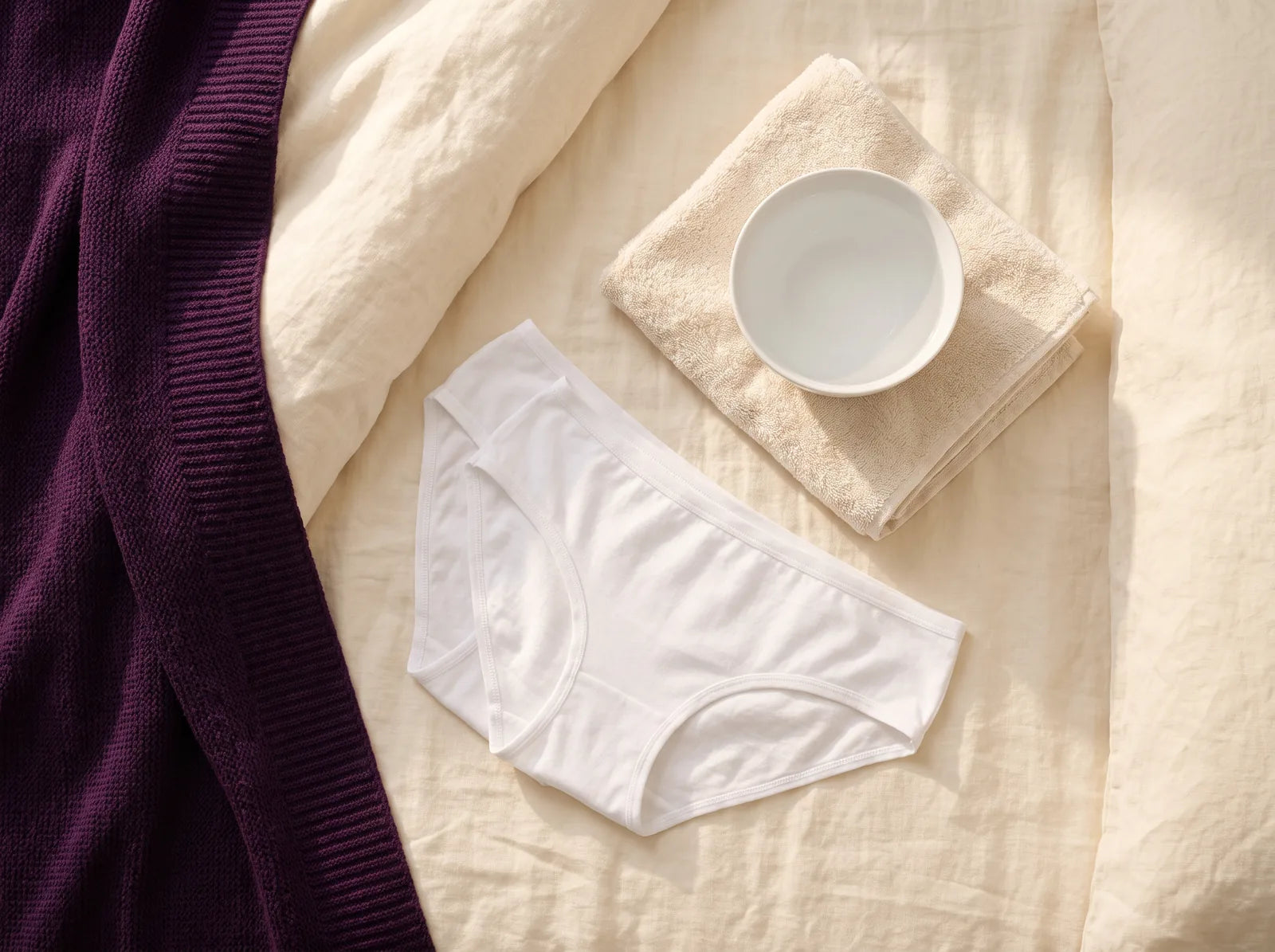 Sfeerbeeld: opgevouwen katoenen onderbroeken, een handdoek en een kom lauw water op bed