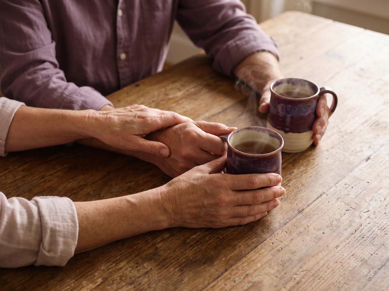 Sfeerbeeld: een vrouw legt haar hand op die van haar partner aan de keukentafel met thee