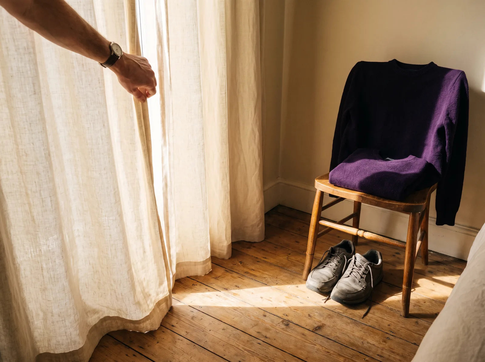 Sfeerbeeld: hand schuift in de ochtend het gordijn open, trui en wandelschoenen liggen klaar