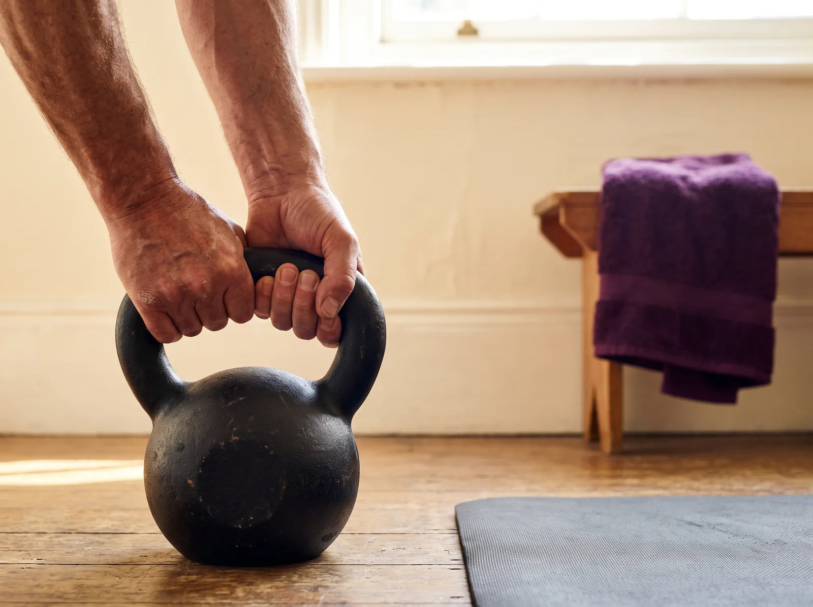 Sfeerbeeld: handen van een oudere man pakken een kettlebell op een houten vloer